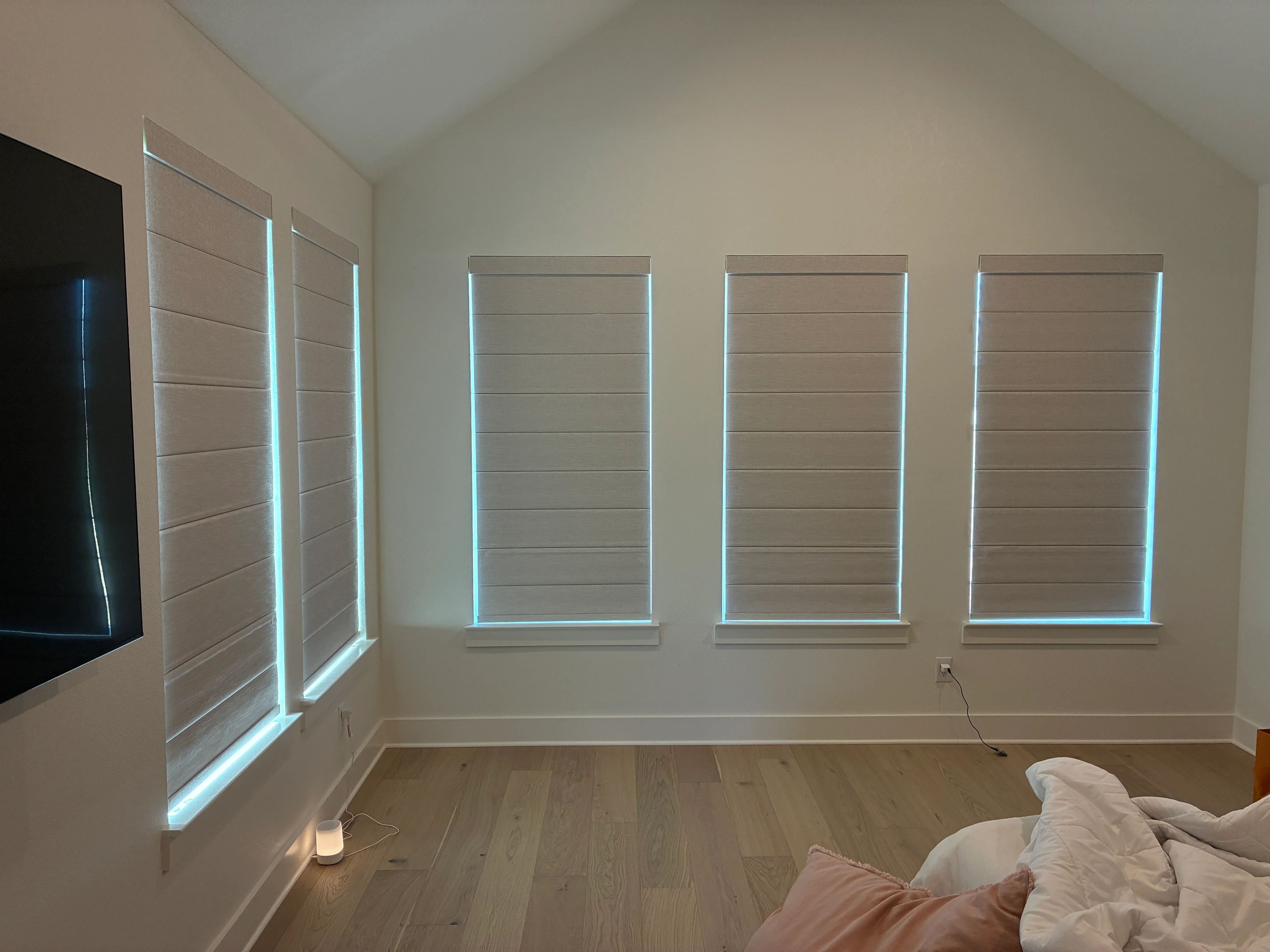 Four motorized roller shades with LED edge lighting installed on bedroom wall