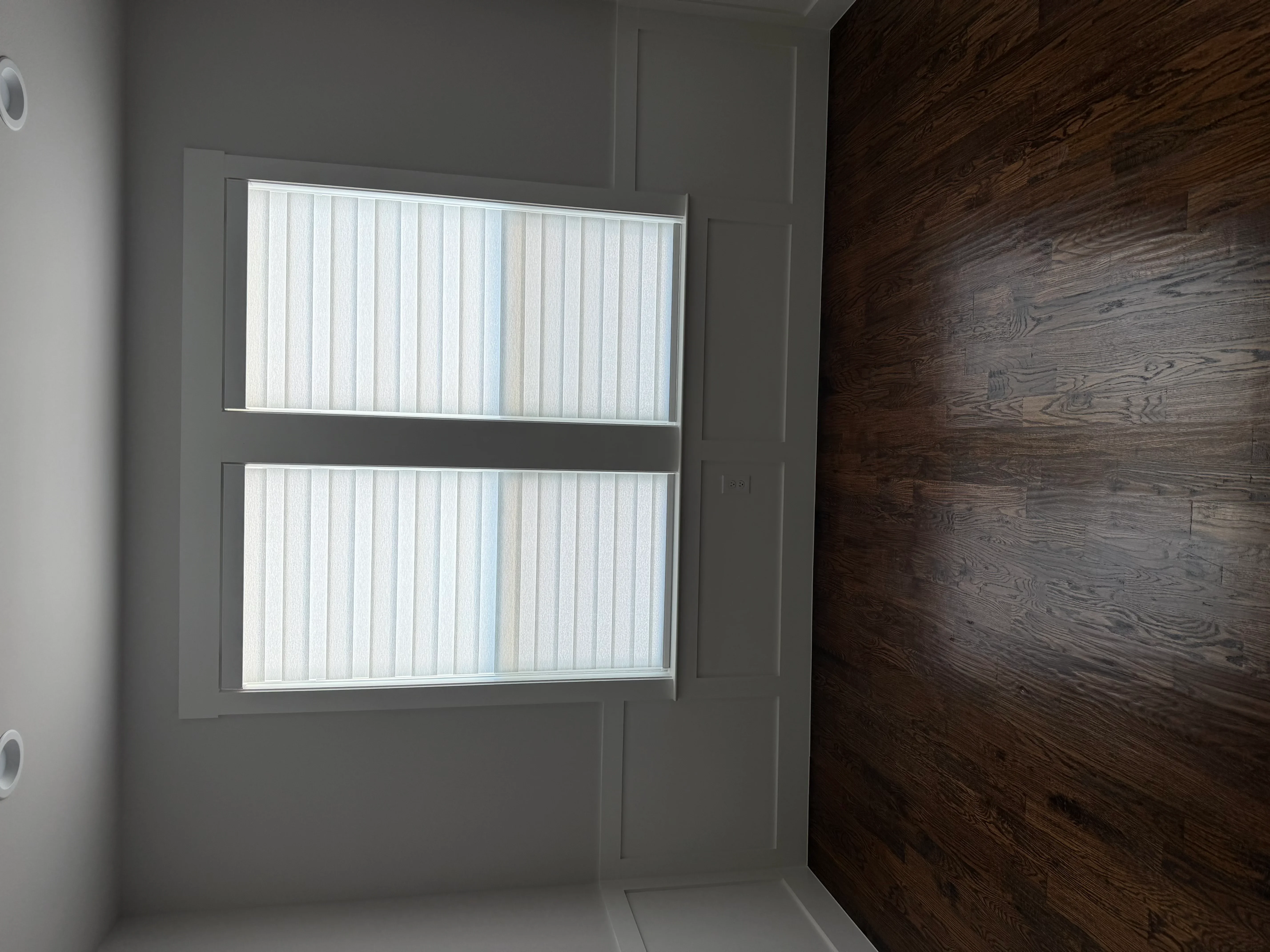 Two large windows with white vertical blinds in aluminum frames, gray drywall finish