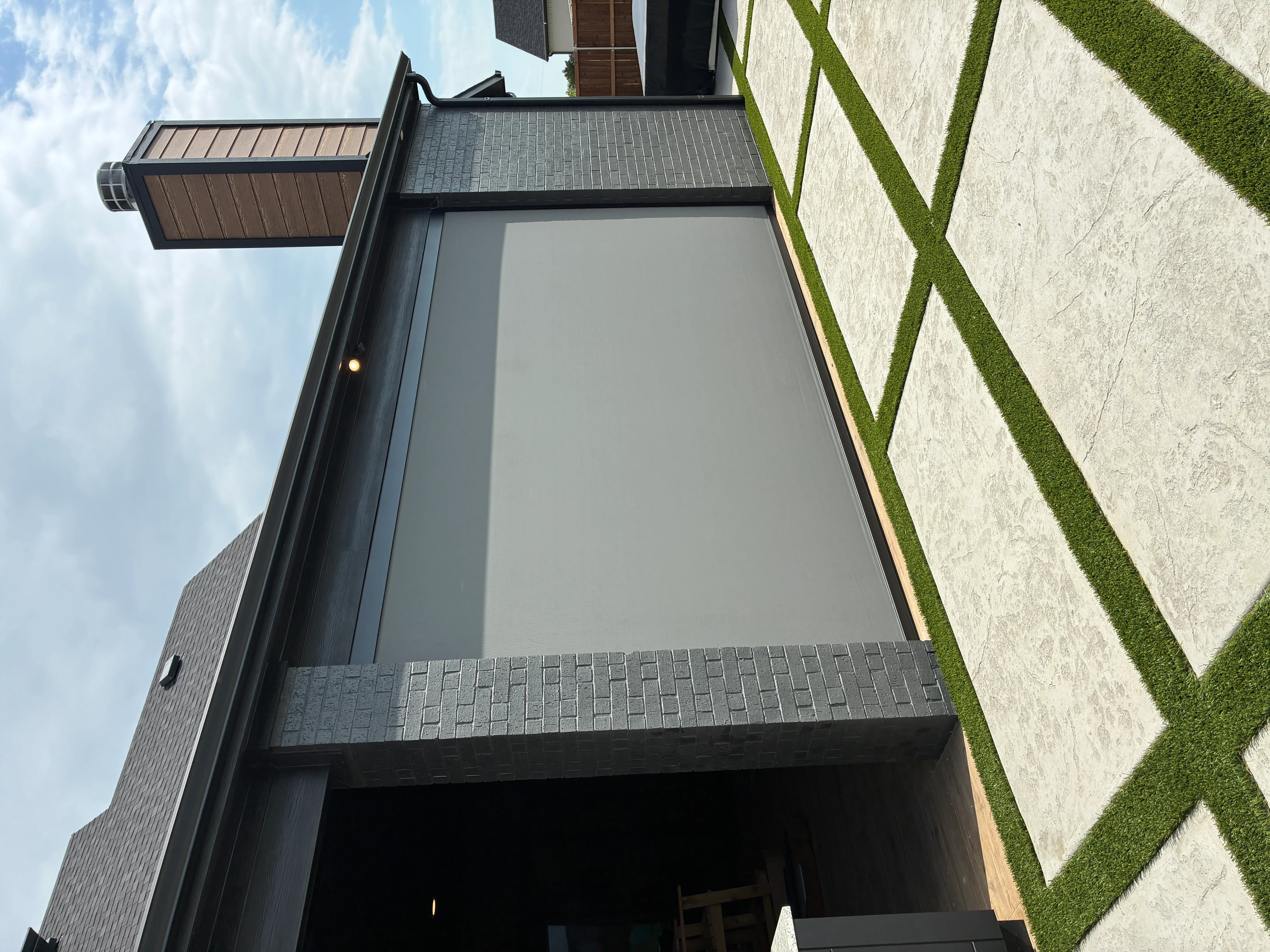 Gray roller shade installed in black aluminum frame on modern home exterior